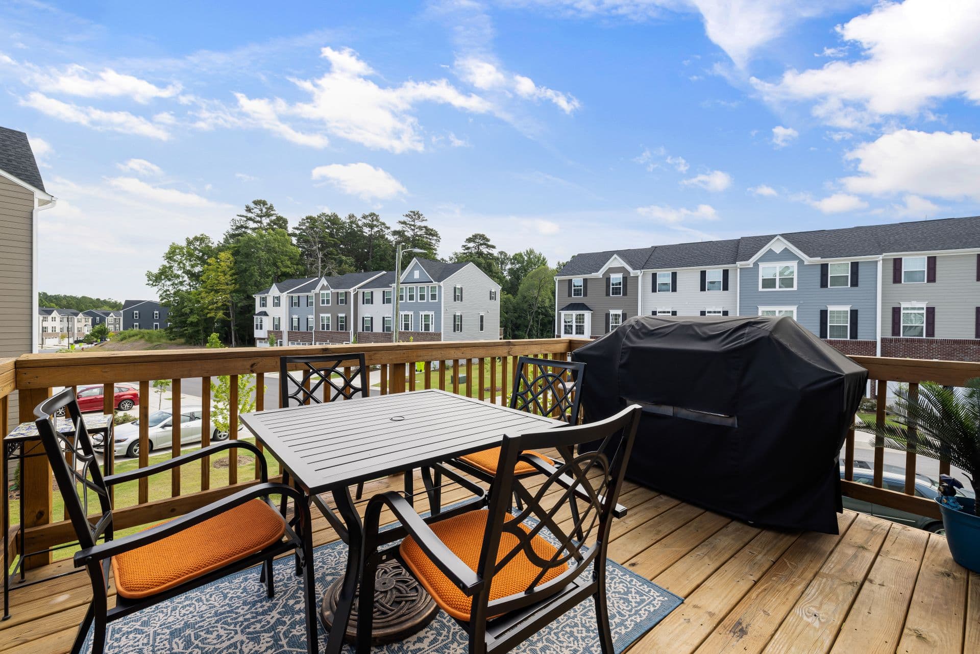 A wooden backyard deck with a railing, a patio table and chairs, and a covered grill