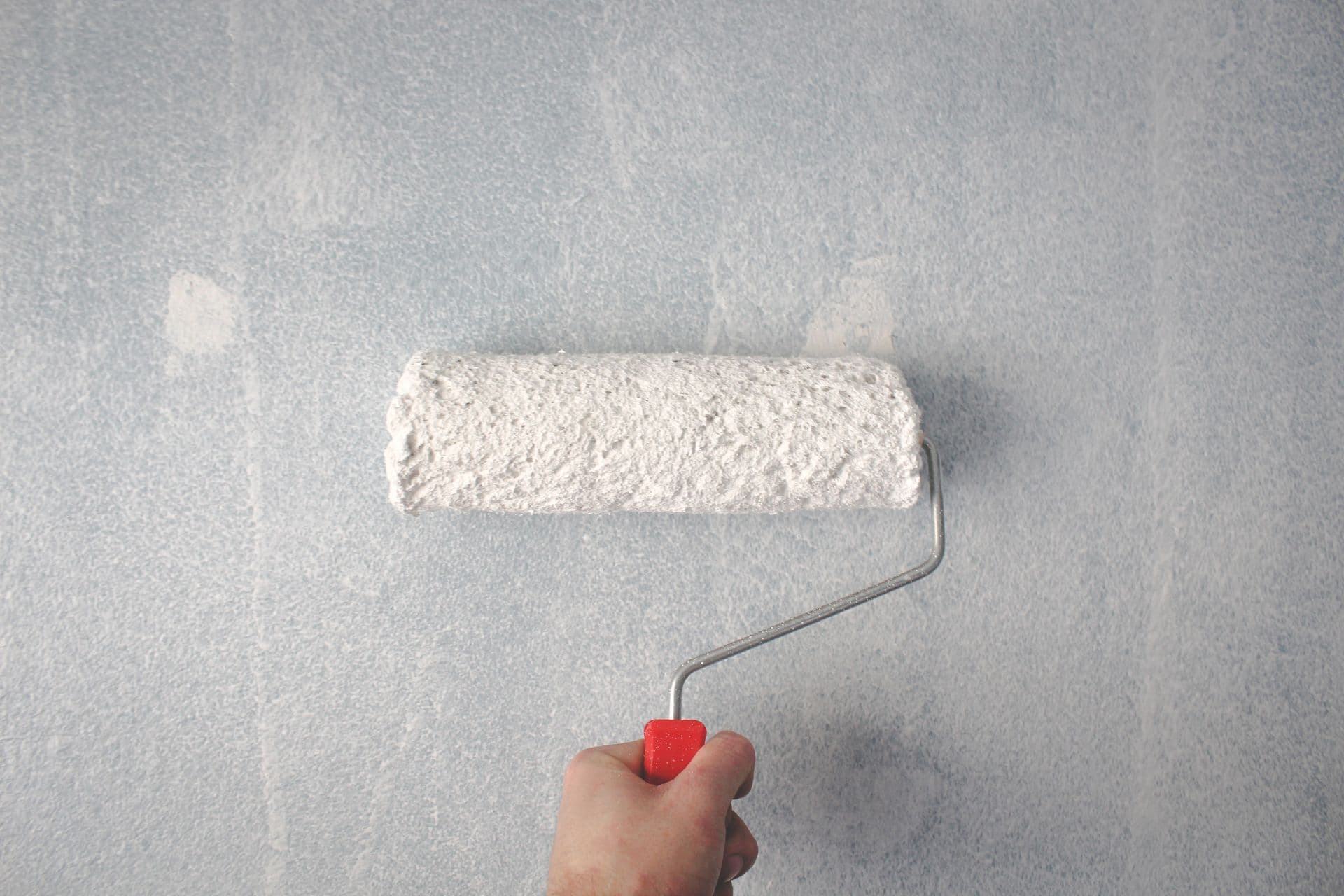 A hand rolling white primer onto a lightly textured wall