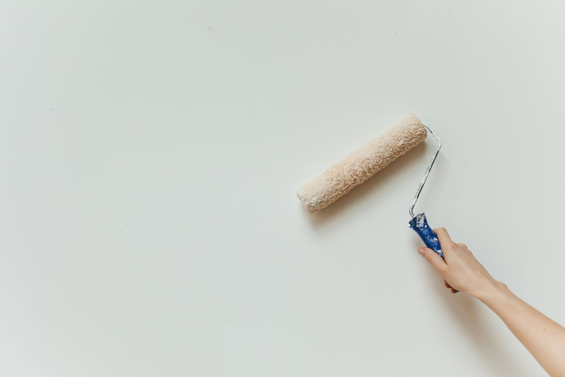 A hand guiding a paint roller across a smooth neutral wall